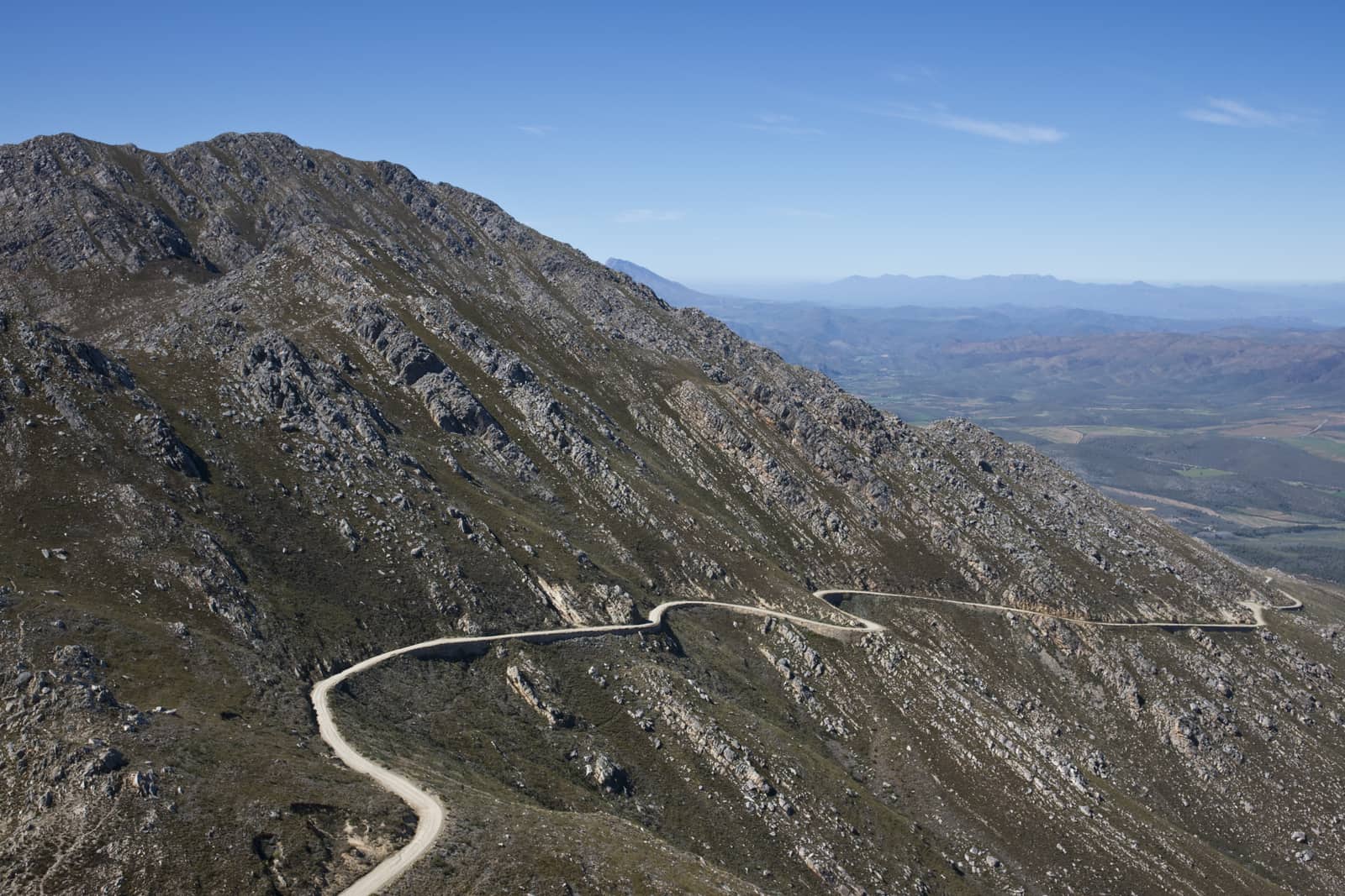 Serpentinen einer Passstraße an einem kahlen Hang, Blick weit ins Land